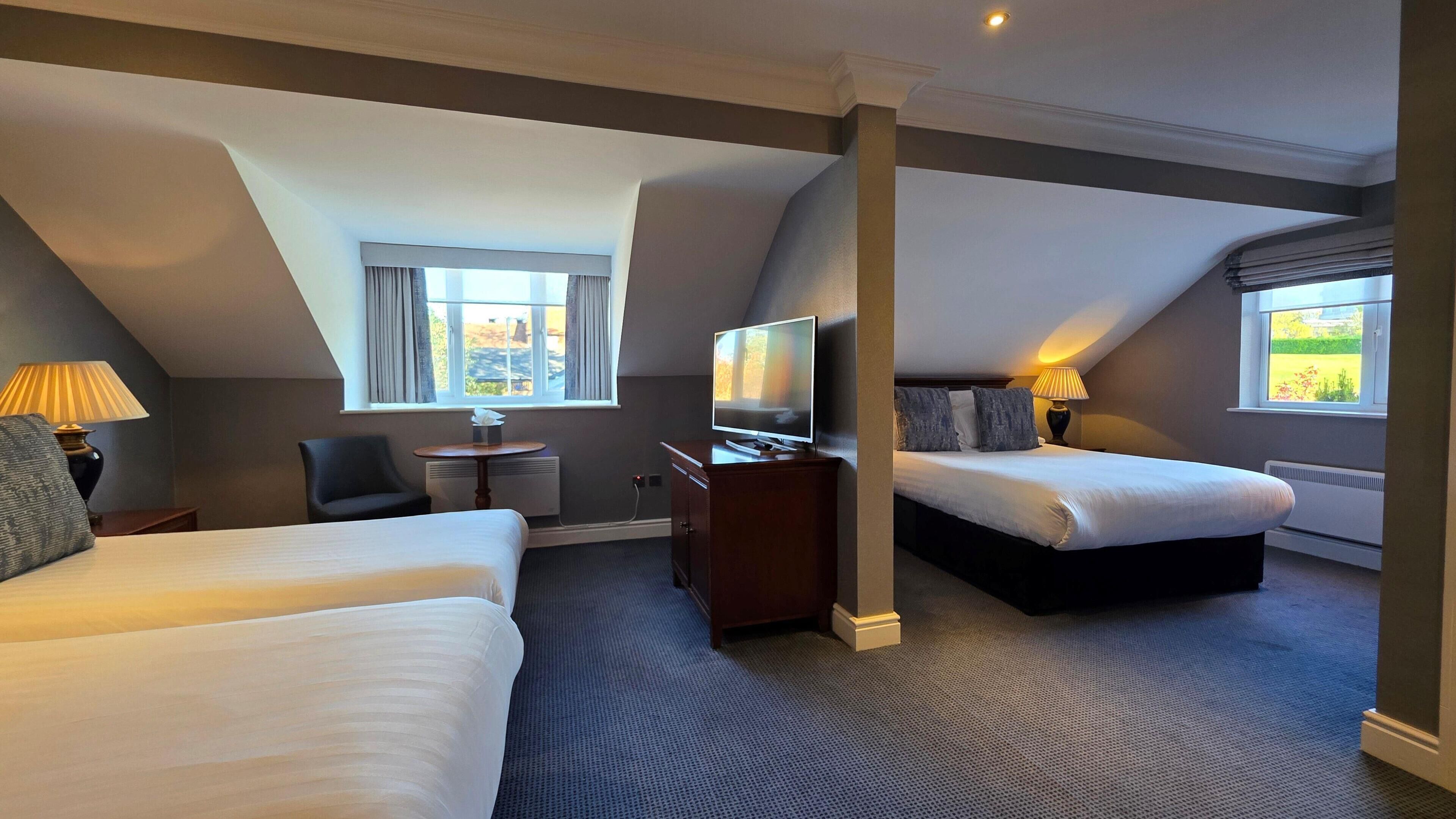 A hotel room with two beds, a desk, a television, and a window with curtains.