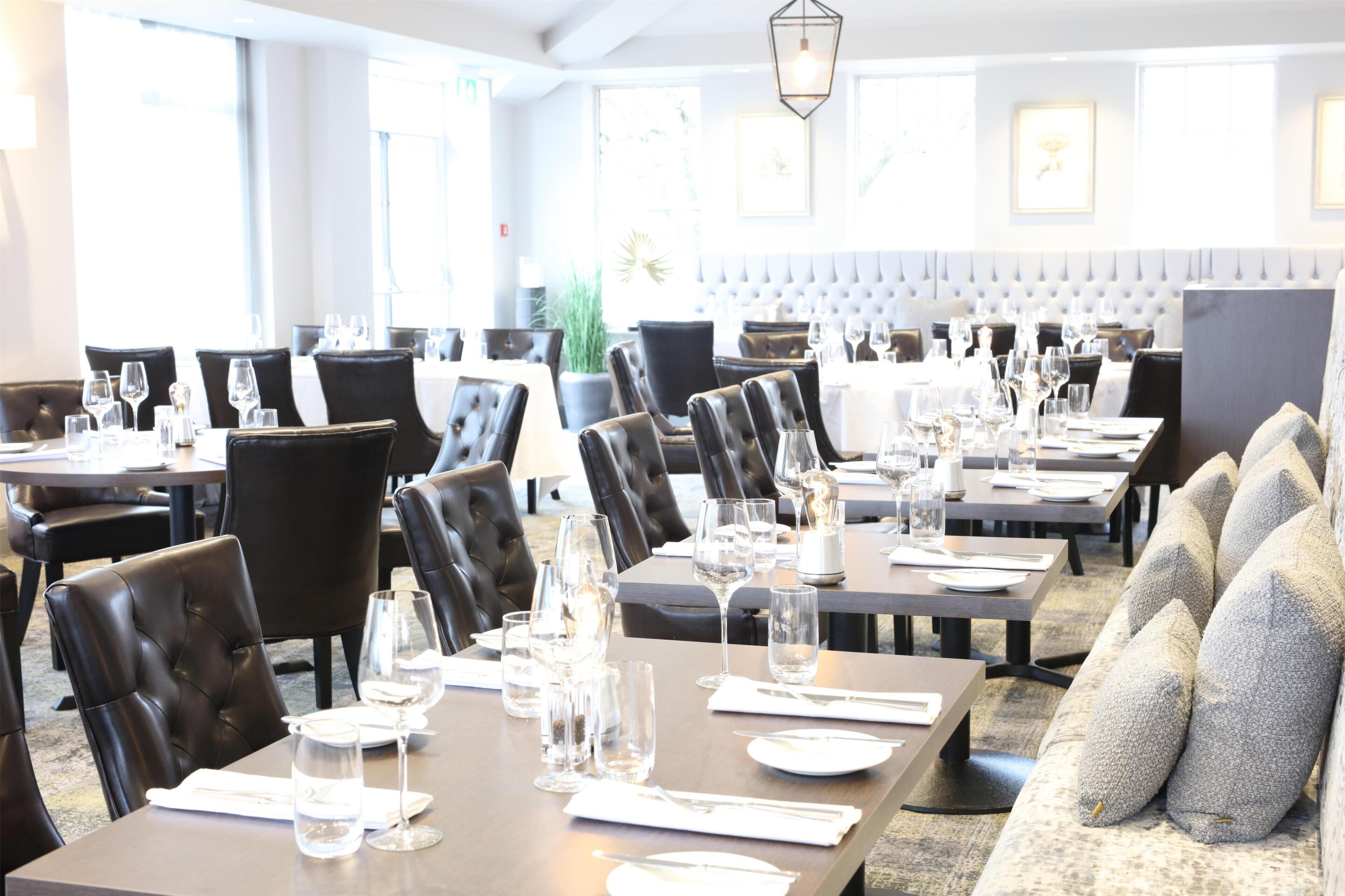 Ein Restaurant mit mehreren Tischen, schwarzen Ledersesseln und einer gepolsterten Bank.