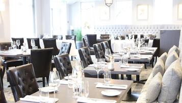 Ein Restaurant mit mehreren Tischen, schwarzen Ledersesseln und einer gepolsterten Bank.