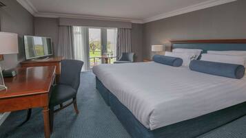 Habitación de hotel con una cama grande, un escritorio con silla, televisión y vistas al exterior a través de una puerta corrediza.