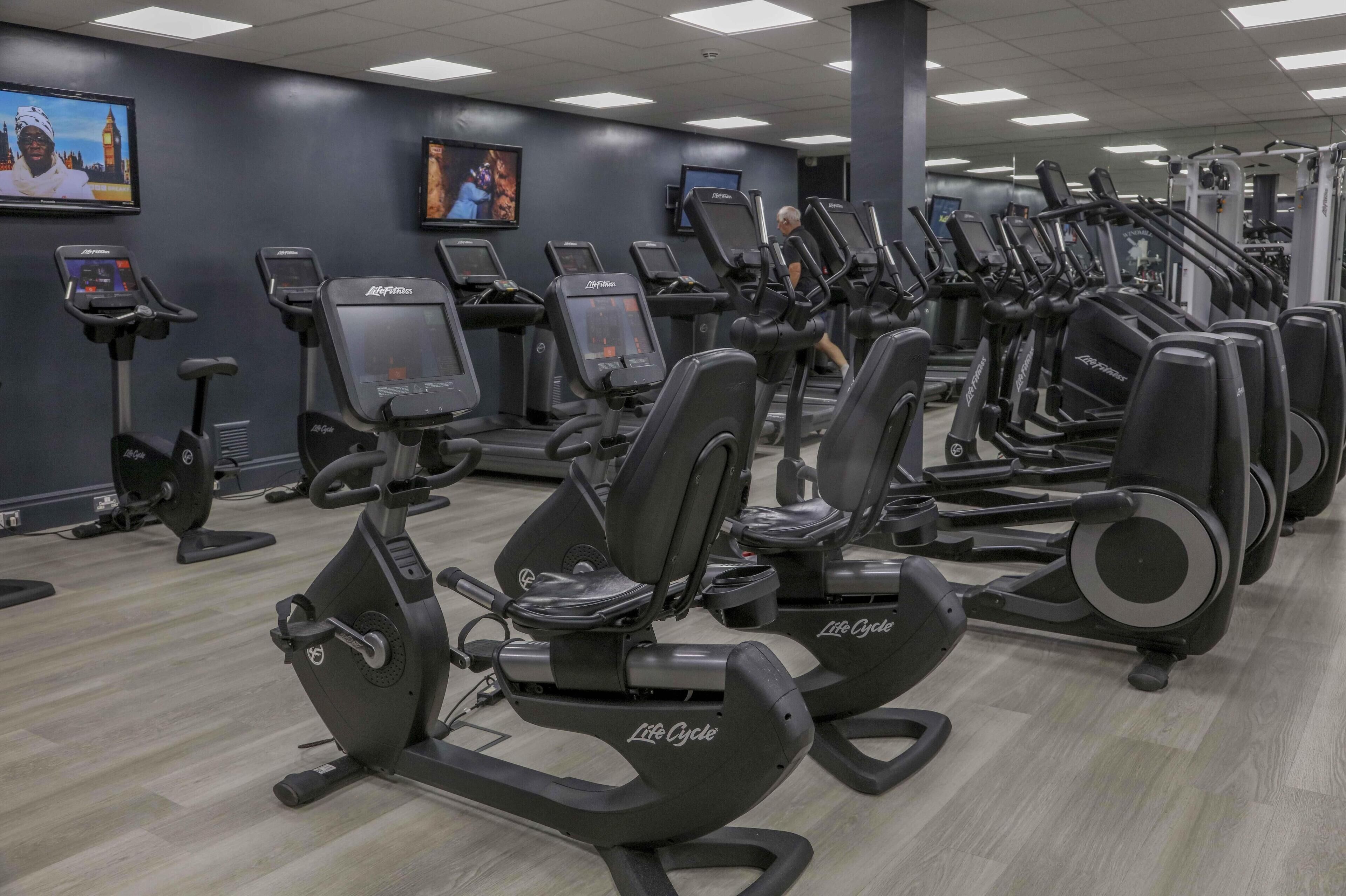 Une salle de sport équipée de nombreux appareils de cardio, notamment des tapis de course et des elliptiques, disposés en rangées.