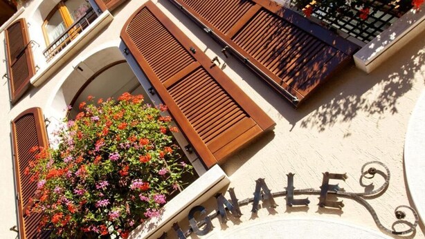 Un edificio con un letrero que dice "BARTHALE" y varios balcones con contraventanas de madera y jardineras con flores.