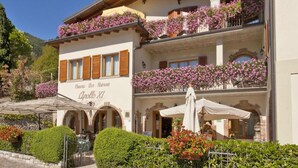 Un edificio de dos pisos con balcones decorados con flores rosadas, un letrero que dice "Apollo RZ" y área de estar al aire libre con sombrillas.