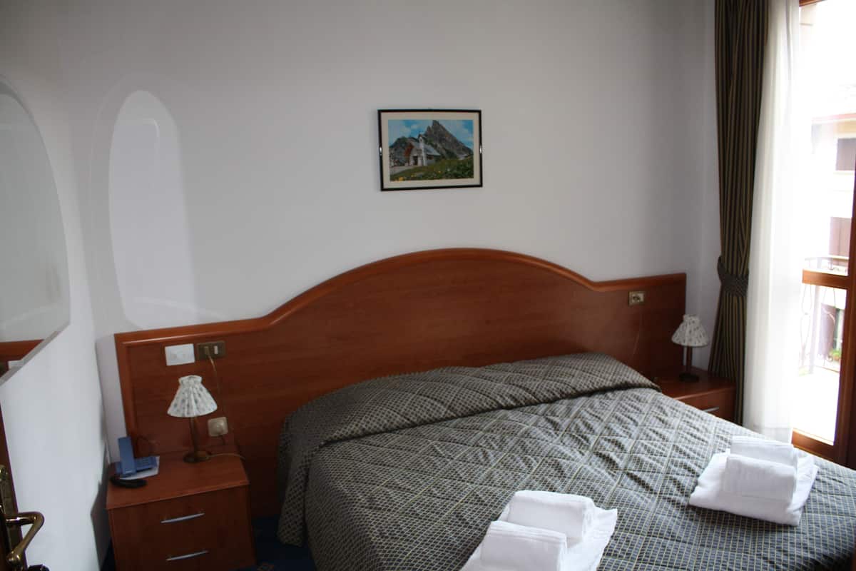 A hotel room with a wooden headboard, a bed with a patterned bedspread, two bedside tables with lamps, and a framed picture on the wall.