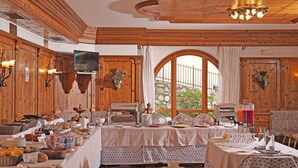 Comedor con mesas de buffet, paredes de madera y un amplio ventanal con vista a un muro de piedra.