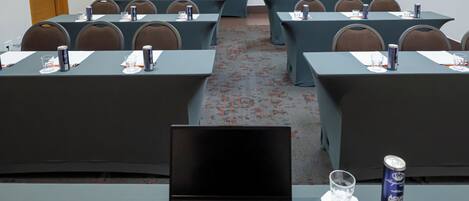 A conference room with multiple tables, each equipped with a laptop, water glass, and a can of drink.