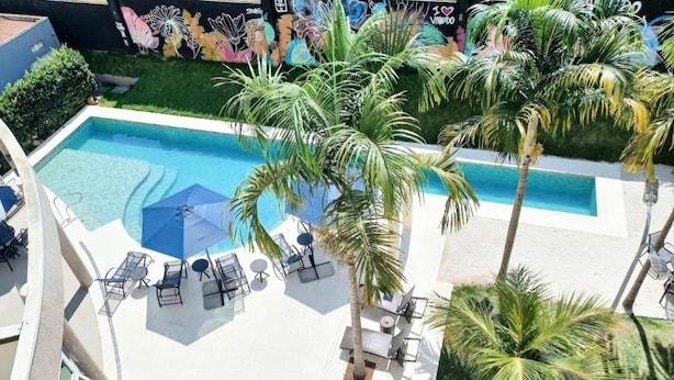 An aerial view of a pool area with palm trees, lounge chairs, and a mural on the wall. - Intercity Vinhedo (Vinhedo)