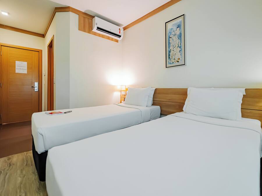 Une chambre d’hôtel avec deux lits, une tête de lit en bois, une table de chevet, un climatiseur fixé au mur et une œuvre d’art encadrée.