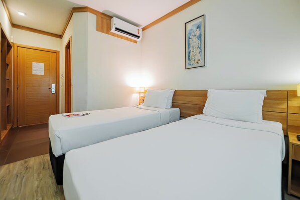 A hotel room with two beds, a wooden headboard, a nightstand, a wall-mounted air conditioner, and a framed artwork. - Intercity Vinhedo (Vinhedo)