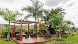 A covered outdoor seating area with wicker furniture, surrounded by palm trees and a stone feature. - Intercity Vinhedo (Vinhedo)