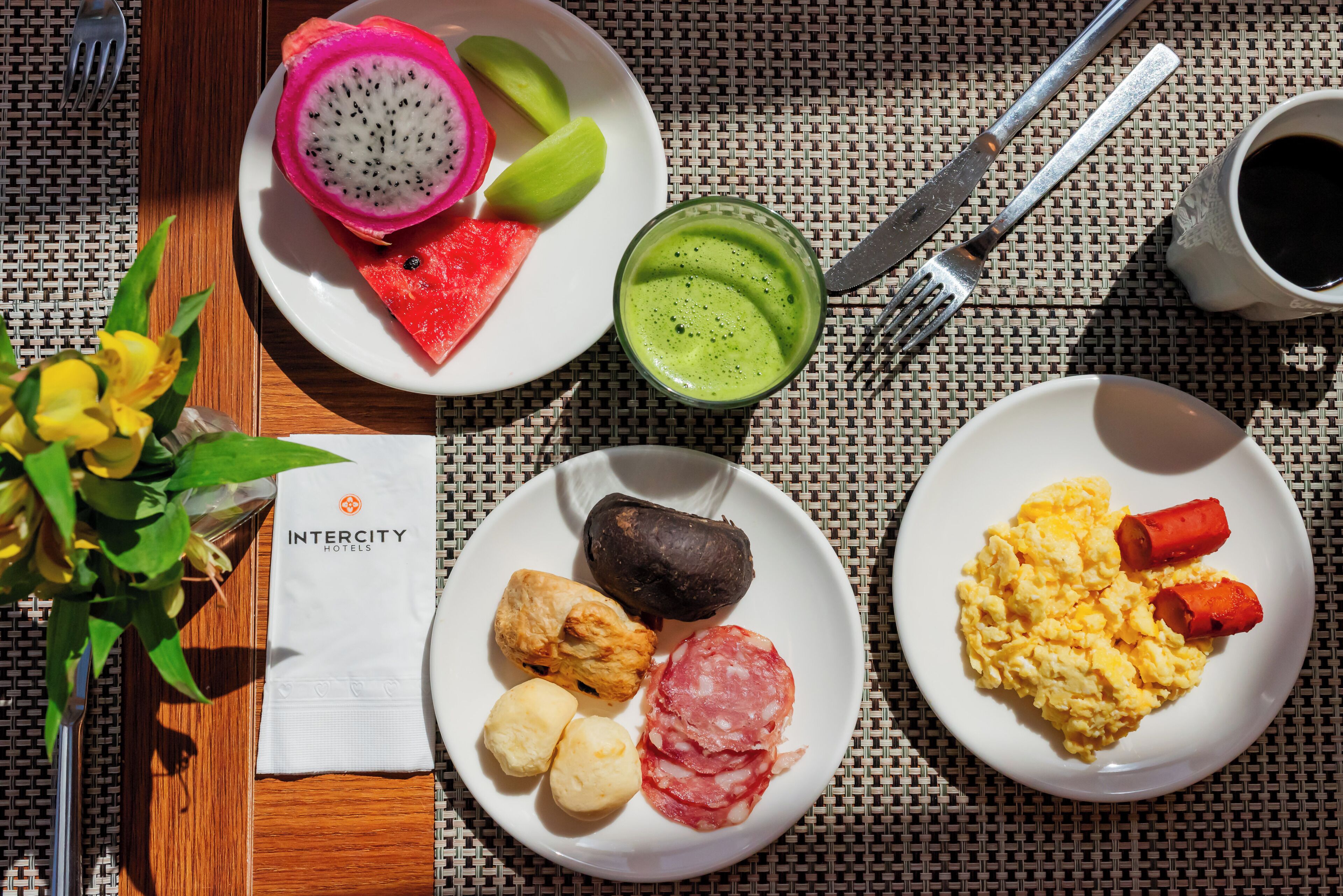 A breakfast setting with plates of food, a drink, and a napkin with the Intercity Hotels logo.