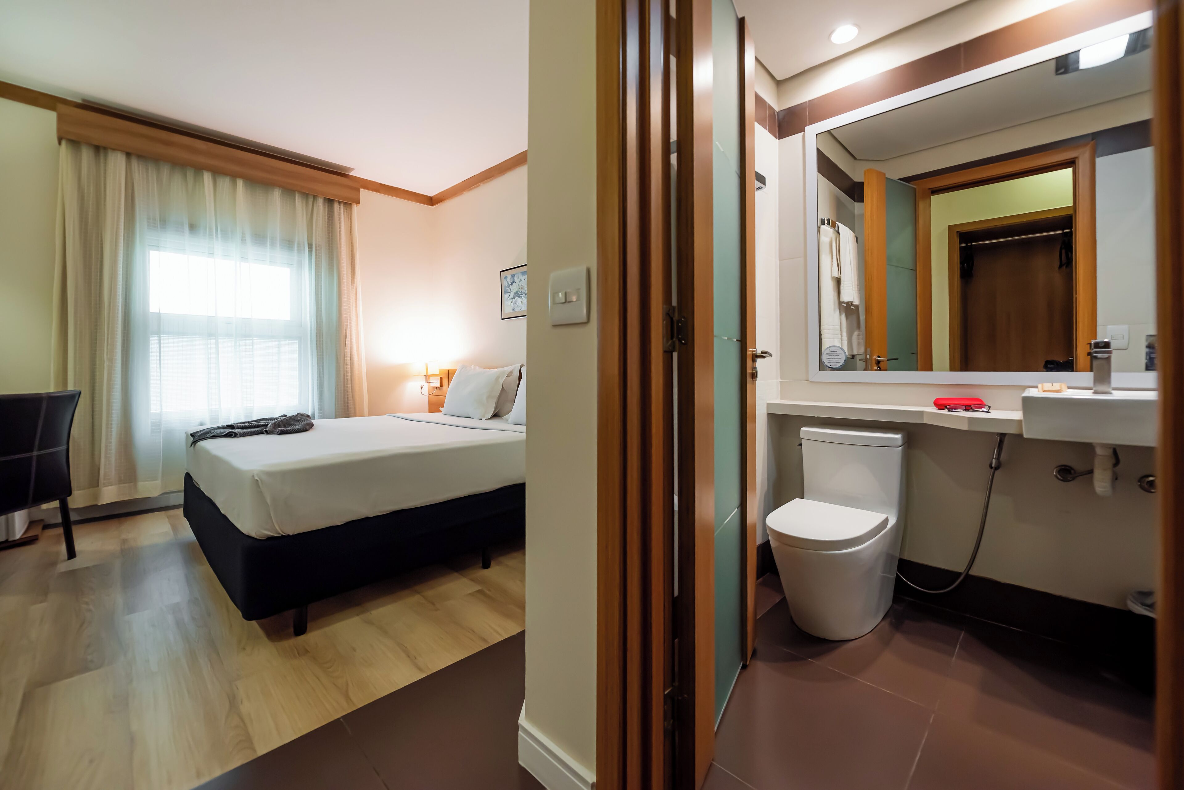 Habitación de hotel con cama, mesita de noche, lámpara y baño con inodoro y lavamanos.