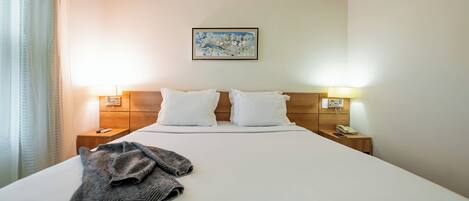 A hotel room with a large bed, two bedside tables with lamps, a painting on the wall, and a window with curtains.