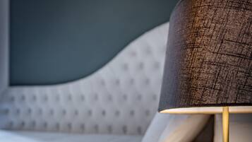 Un lit avec une literie blanche, une table d’appoint ronde à la surface texturée et une lampe avec un abat-jour foncé.