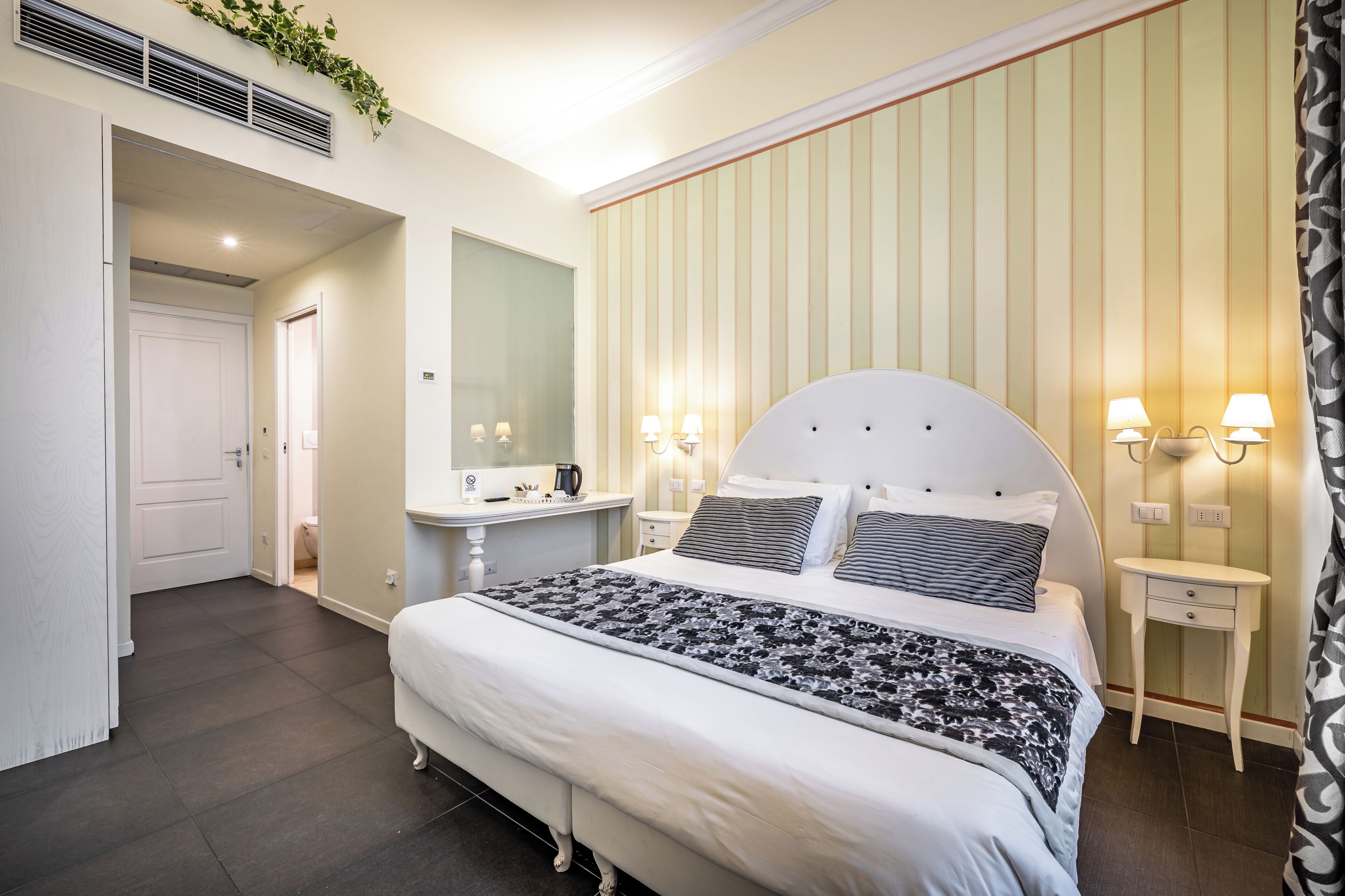 Quarto com cama, mesas de cabeceira, espelho e luminária na parede.
