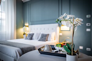 A hotel room with a bed, bedside table, and a potted orchid.