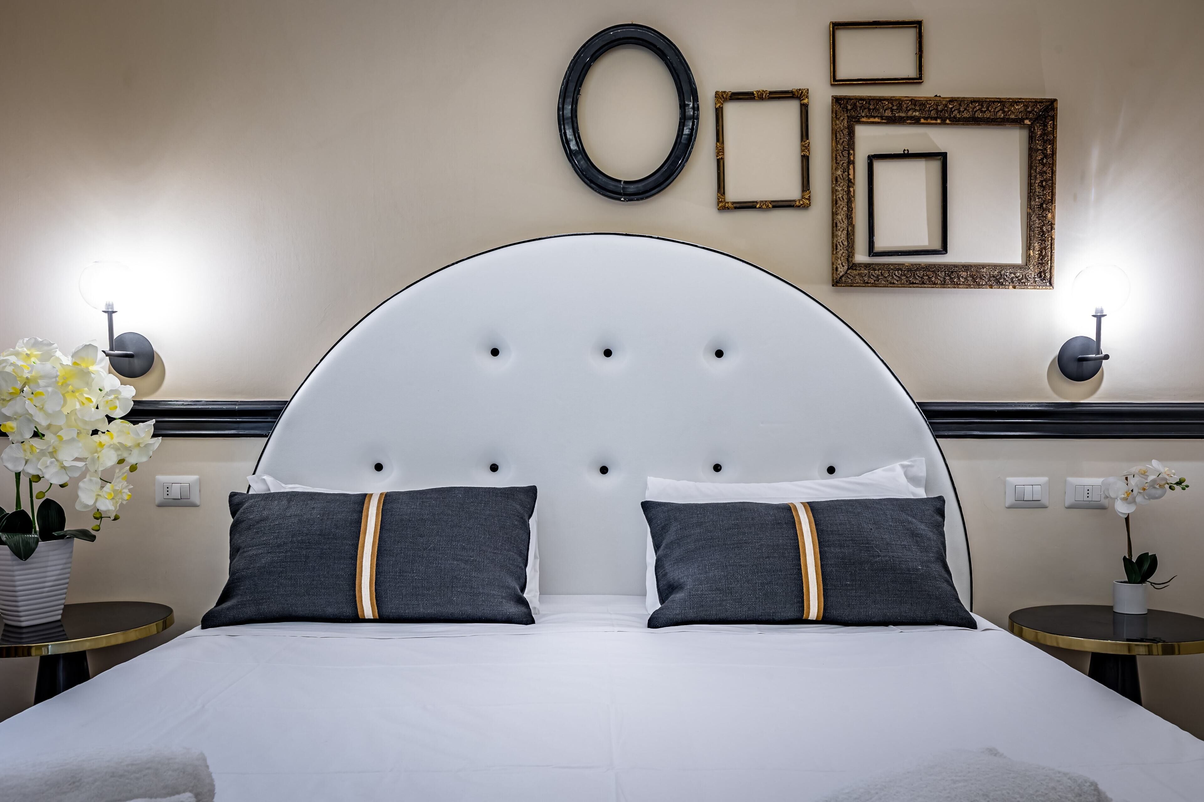 A hotel room with a large bed, two bedside tables, a wall-mounted lamp, and a potted plant.