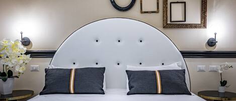 A hotel room with a large bed, two bedside tables, a wall-mounted lamp, and a potted plant.