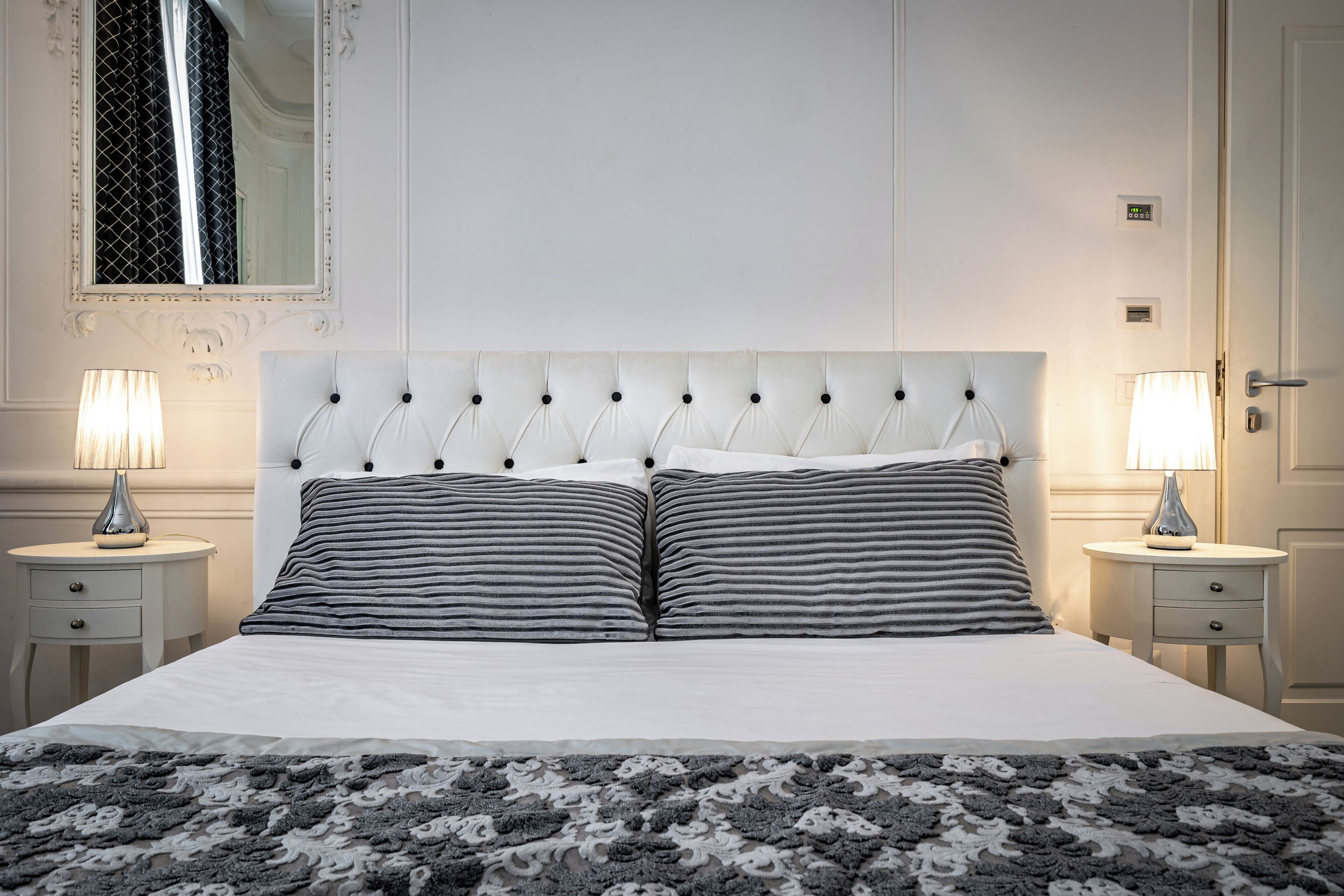 A neatly made bed with a tufted headboard, two bedside tables with lamps, and a patterned rug.
