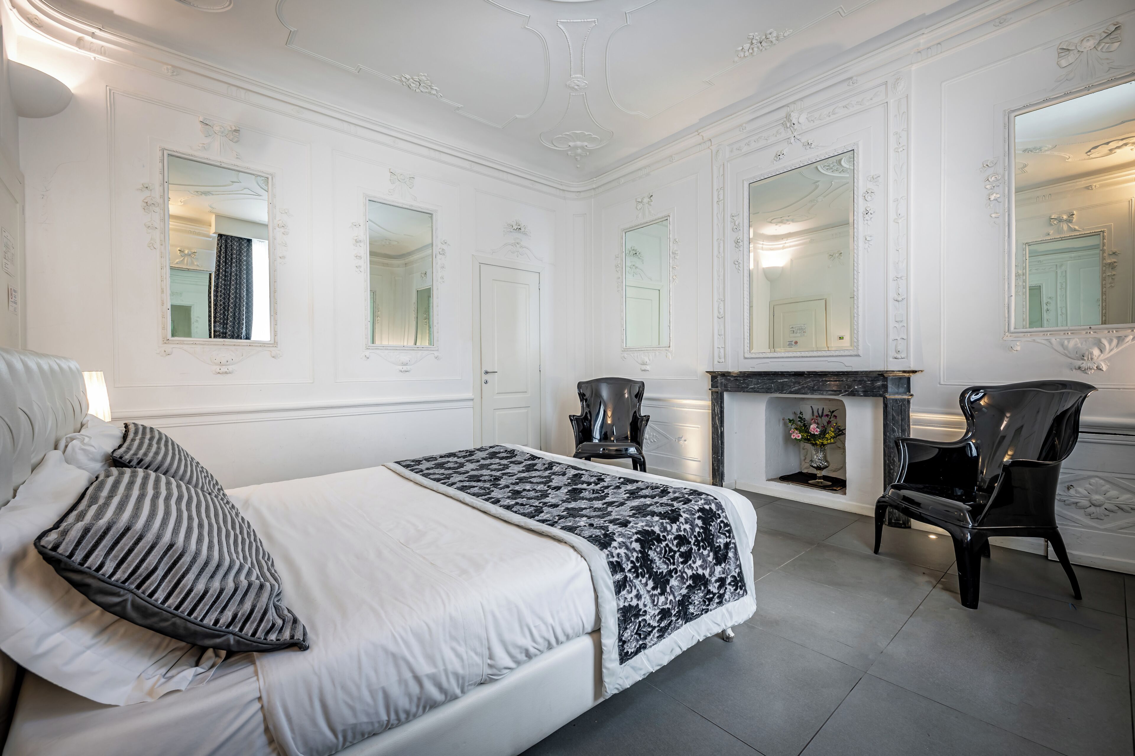 Ein Schlafzimmer mit einem Bett, zwei Stühlen, einem Kamin und einem Spiegel.