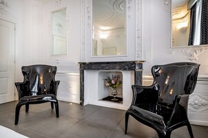 A room with two black chairs, a fireplace, and a mirror on the wall.