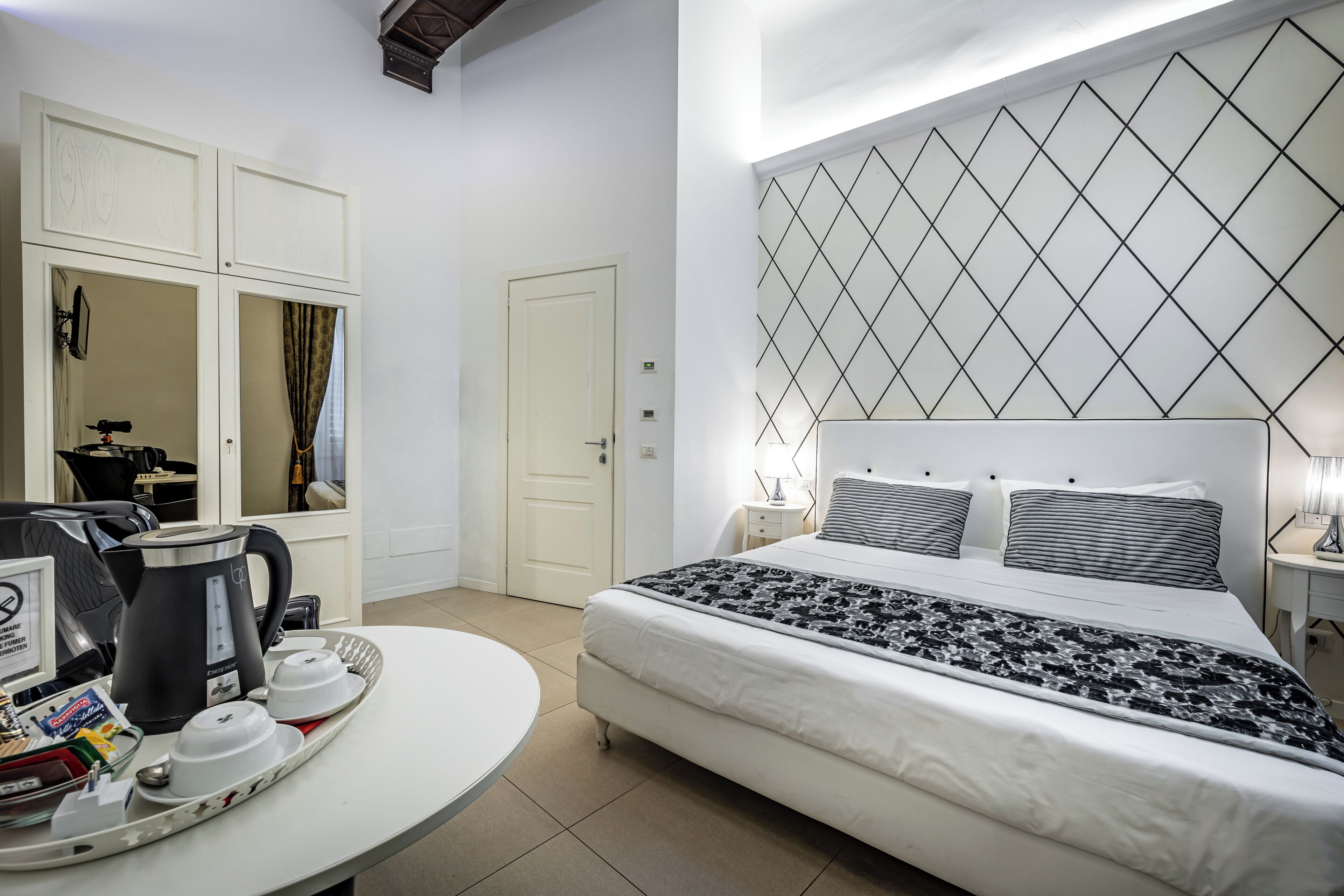 Une chambre d’hôtel équipée d’un lit, d’un coin café, d’une armoire et d’un mur orné d’un motif géométrique.