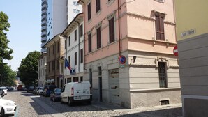 Une vue de rue avec des voitures garées, un bâtiment portant une enseigne indiquant « VIA TIBINI » et un panneau interdisant le stationnement.