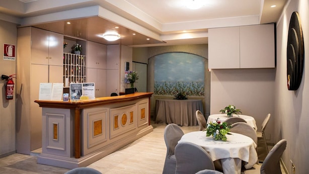 Un espace d’accueil d’hôtel comprenant un comptoir en bois, un extincteur, un bureau de réception et un coin repas avec des tables et des chaises.