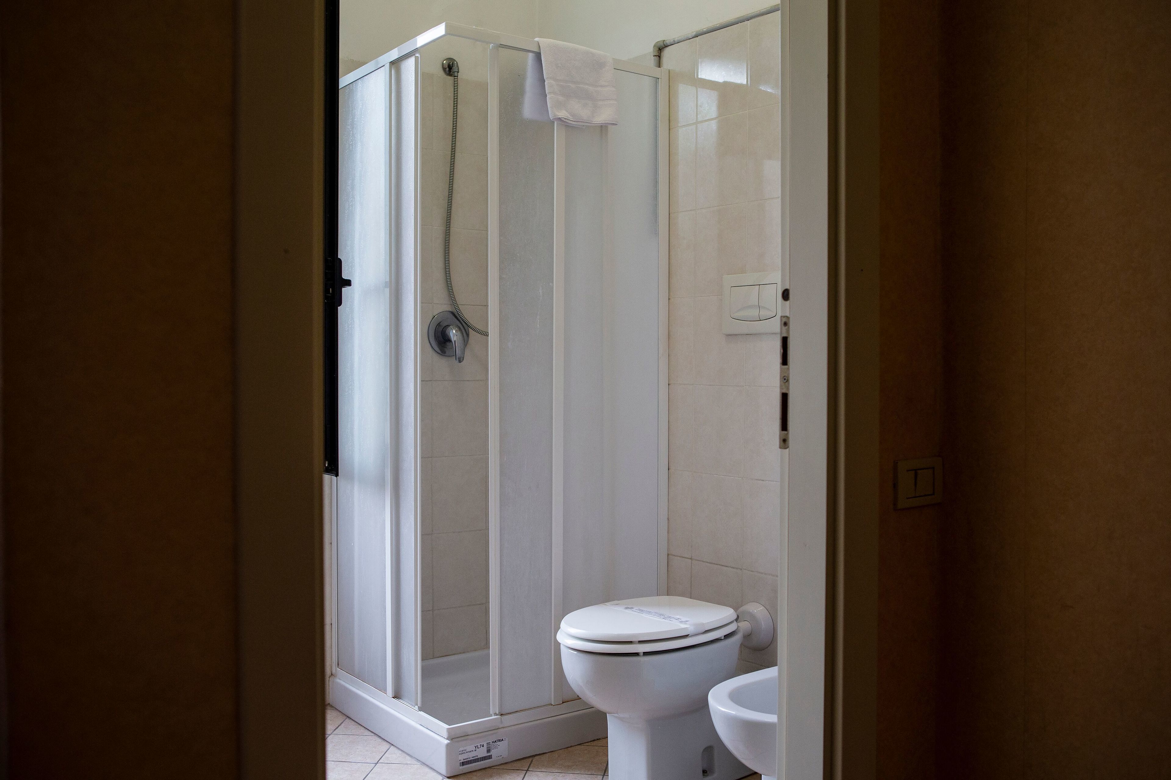Casa de banho com chuveiro separado por vidro, sanita e toalha pendurada na porta do chuveiro.