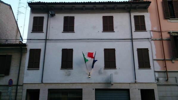 A building with multiple windows and shutters, a no parking sign, and three flags.