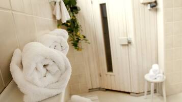 Un baño con paredes de azulejos blancos, una bañera blanca y un taburete pequeño también blanco con toallas.