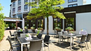 An outdoor patio area with tables and chairs, a tree, and potted plants. - Lobinger Hotel Parkhotel (Giengen an der Brenz)