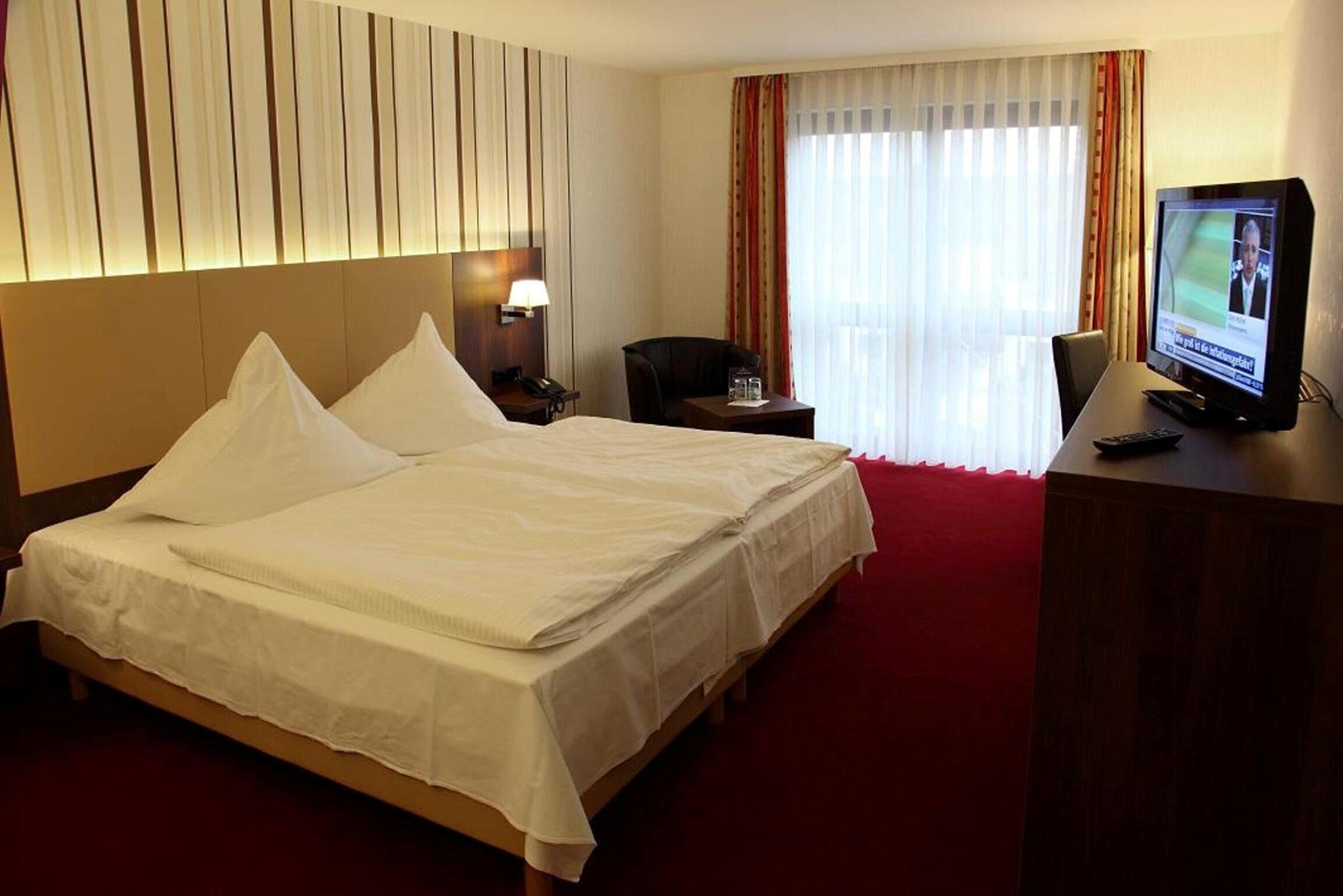 Ein Hotelzimmer mit einem großen Bett, einem Schreibtisch mit Fernseher, einem Sessel und einem Nachttisch.
