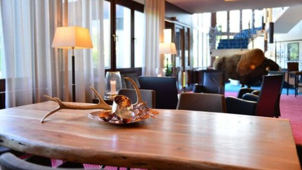 A dining area with a wooden table, two lamps, and a decorative antler centerpiece. - Lobinger Hotel Parkhotel (Giengen an der Brenz)