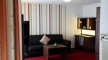 Habitación de hotel con un sofá negro, una mesita de madera, un minibar y un radiador.