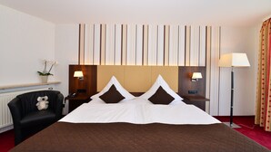 A hotel room with a large bed, a chair, a bedside table with a lamp, and a wall with vertical stripes. - Lobinger Hotel Parkhotel (Giengen an der Brenz)