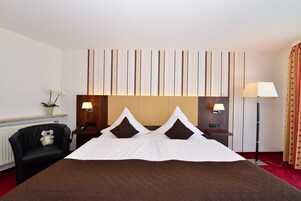 Une chambre d’hôtel avec un grand lit, une chaise, une table de chevet avec une lampe et un mur à rayures verticales.