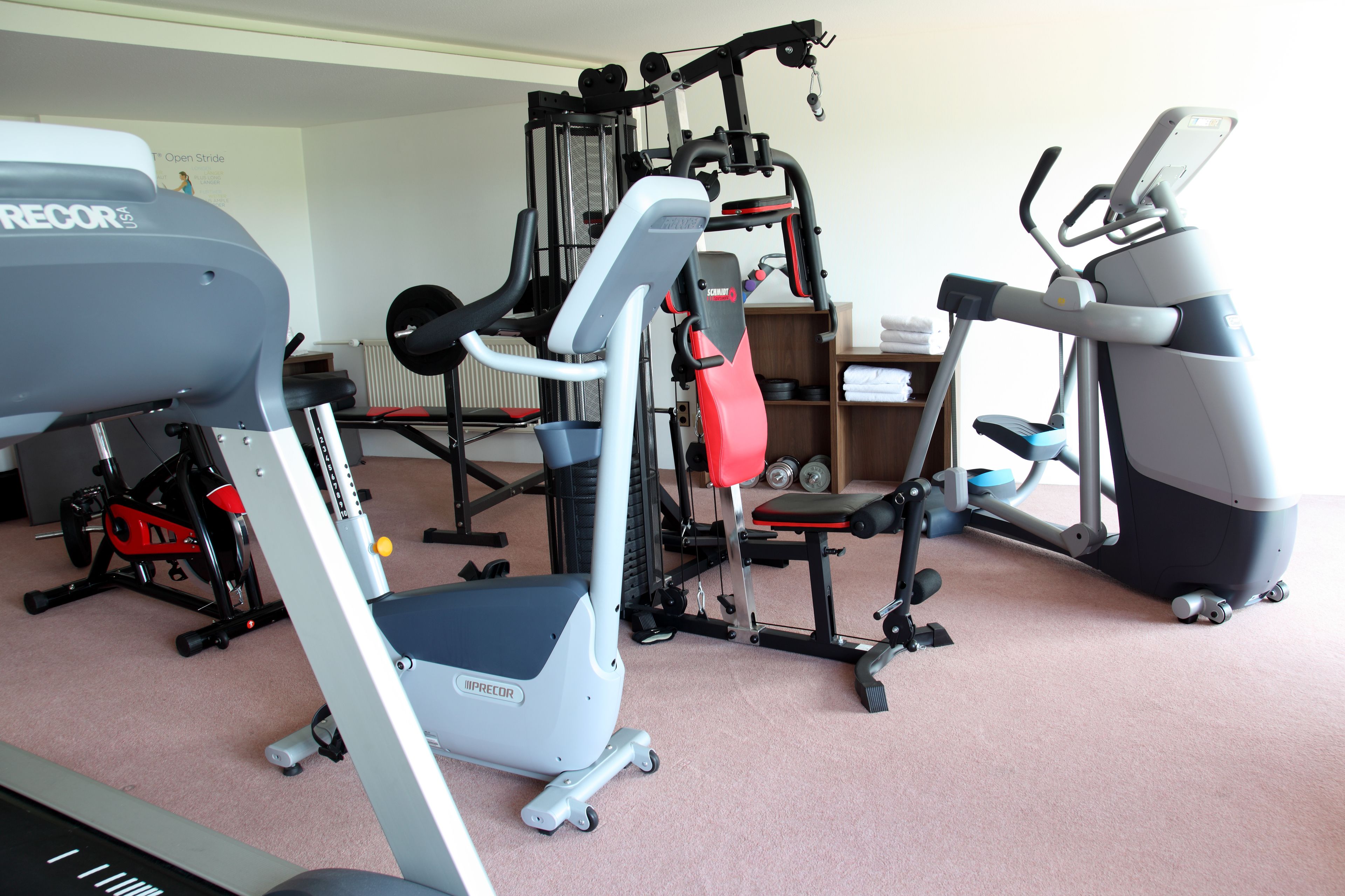 Un gimnasio en casa con varios equipos de ejercicio, incluyendo una caminadora, banco de pesas y una máquina de entrenamiento multifuncional.