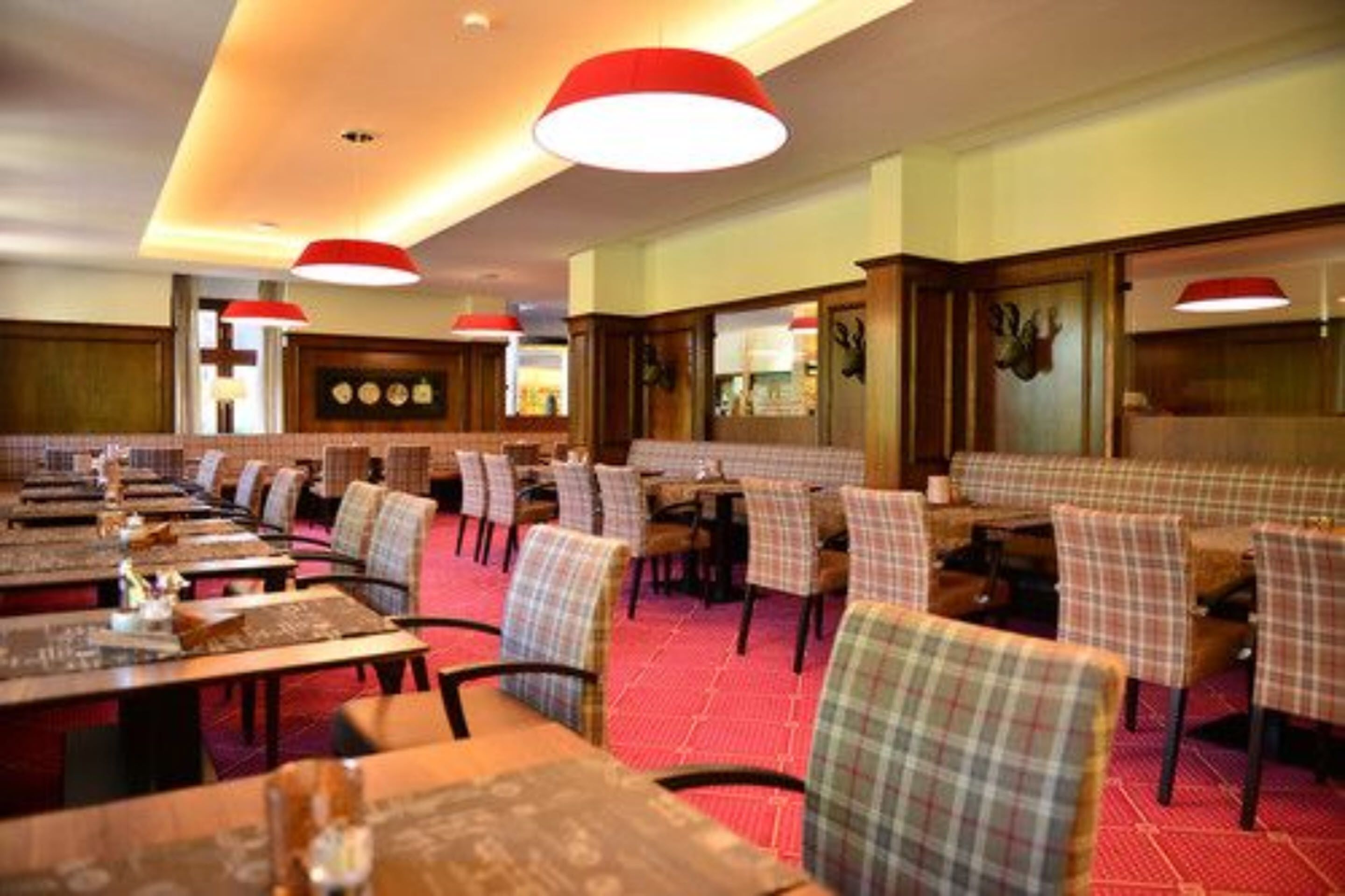 Un restaurant doté de longues tables communes et de banquettes, d’un sol recouvert de moquette rouge et d’un éclairage suspendu.