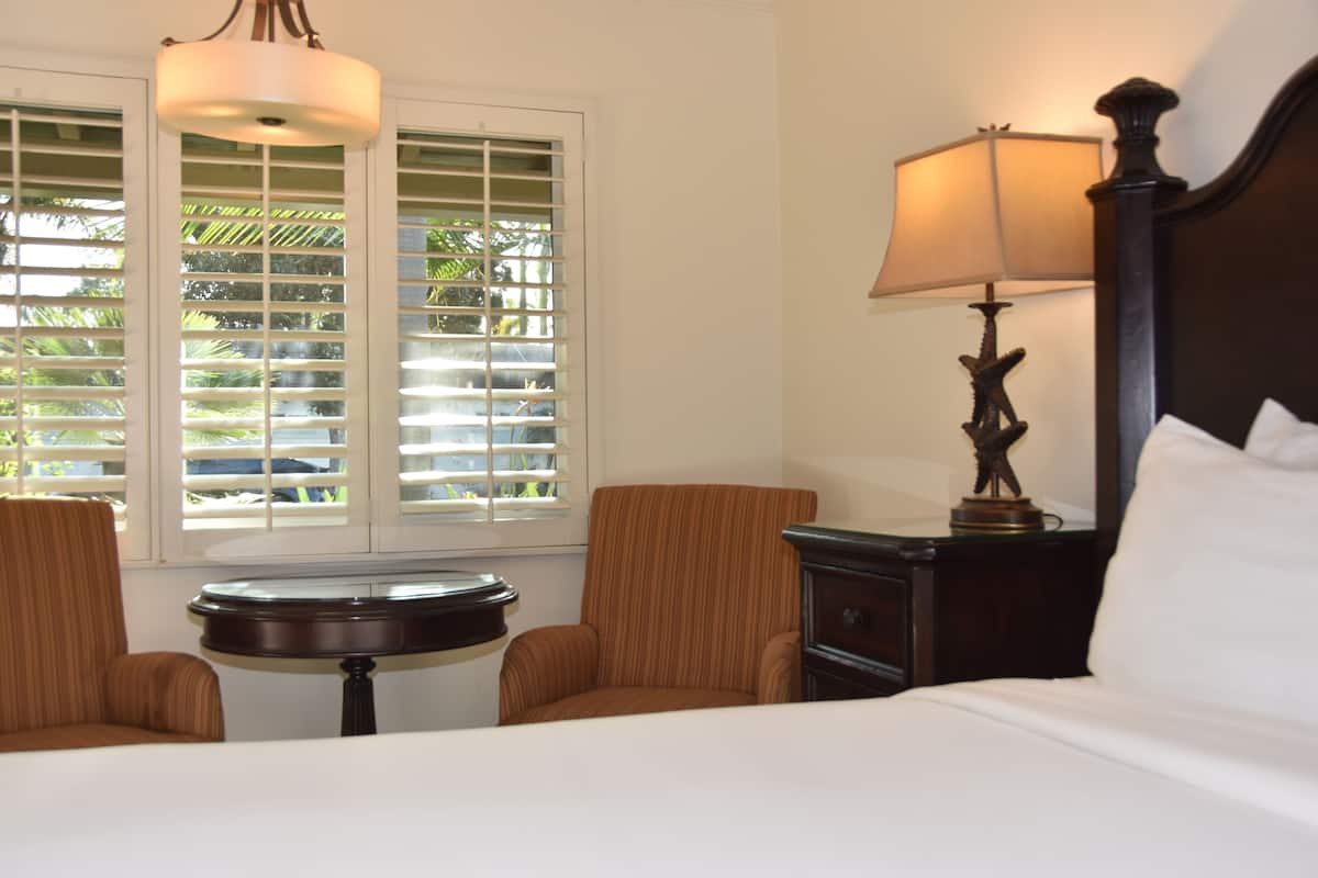 A hotel room with a bed, two armchairs, a small table, a lamp, and a window with blinds.