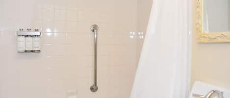 A bathroom with a bathtub, a shower with a grab bar, a sink with a mirror, and toiletries on the wall.