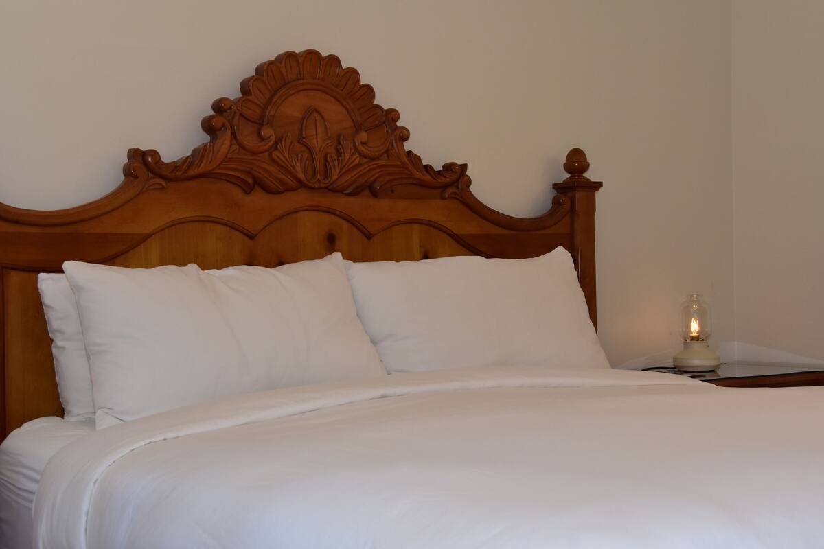 A neatly made bed with white linens and a wooden headboard with intricate carvings.