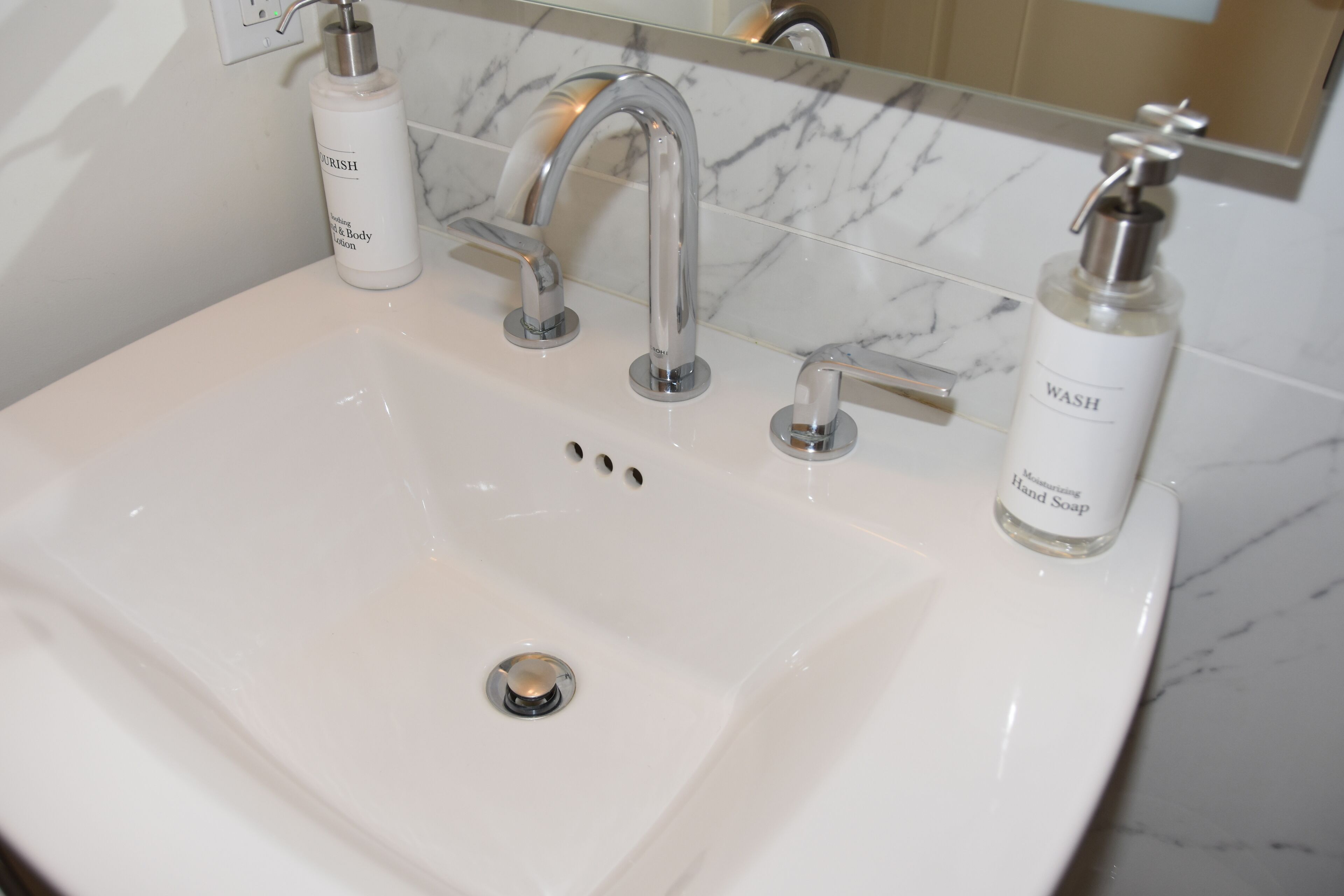 A white bathroom sink with a modern faucet and two soap dispensers labeled "WASH" and "FLOURISH".
