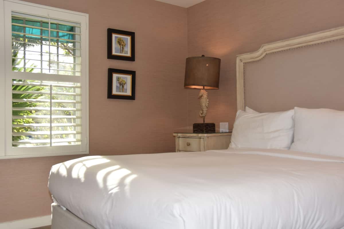 A neatly made bed with white linens, a bedside lamp, and two framed pictures on the wall.