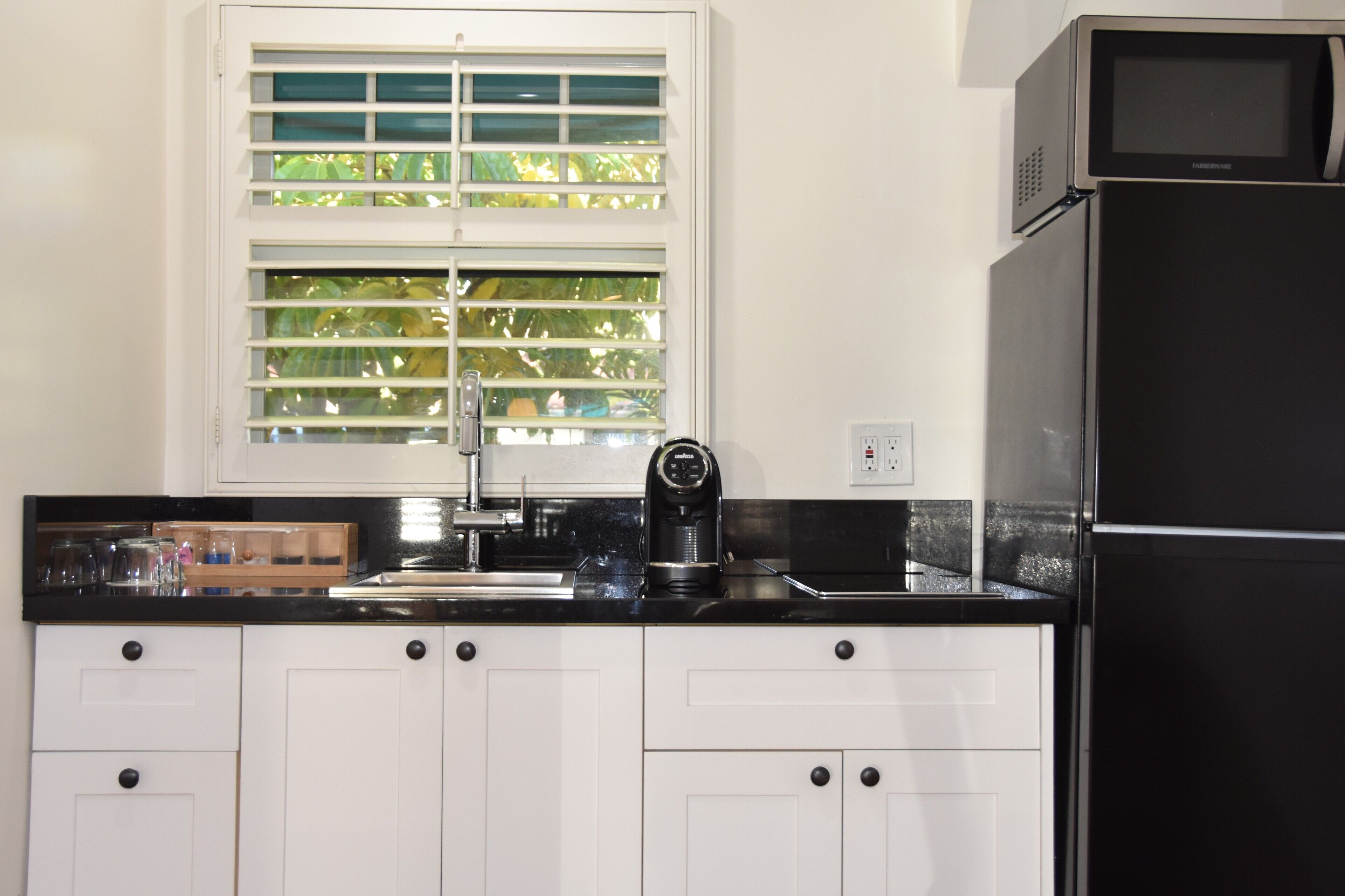 A kitchen with white cabinets, a black refrigerator, a coffee maker, and a window with blinds.