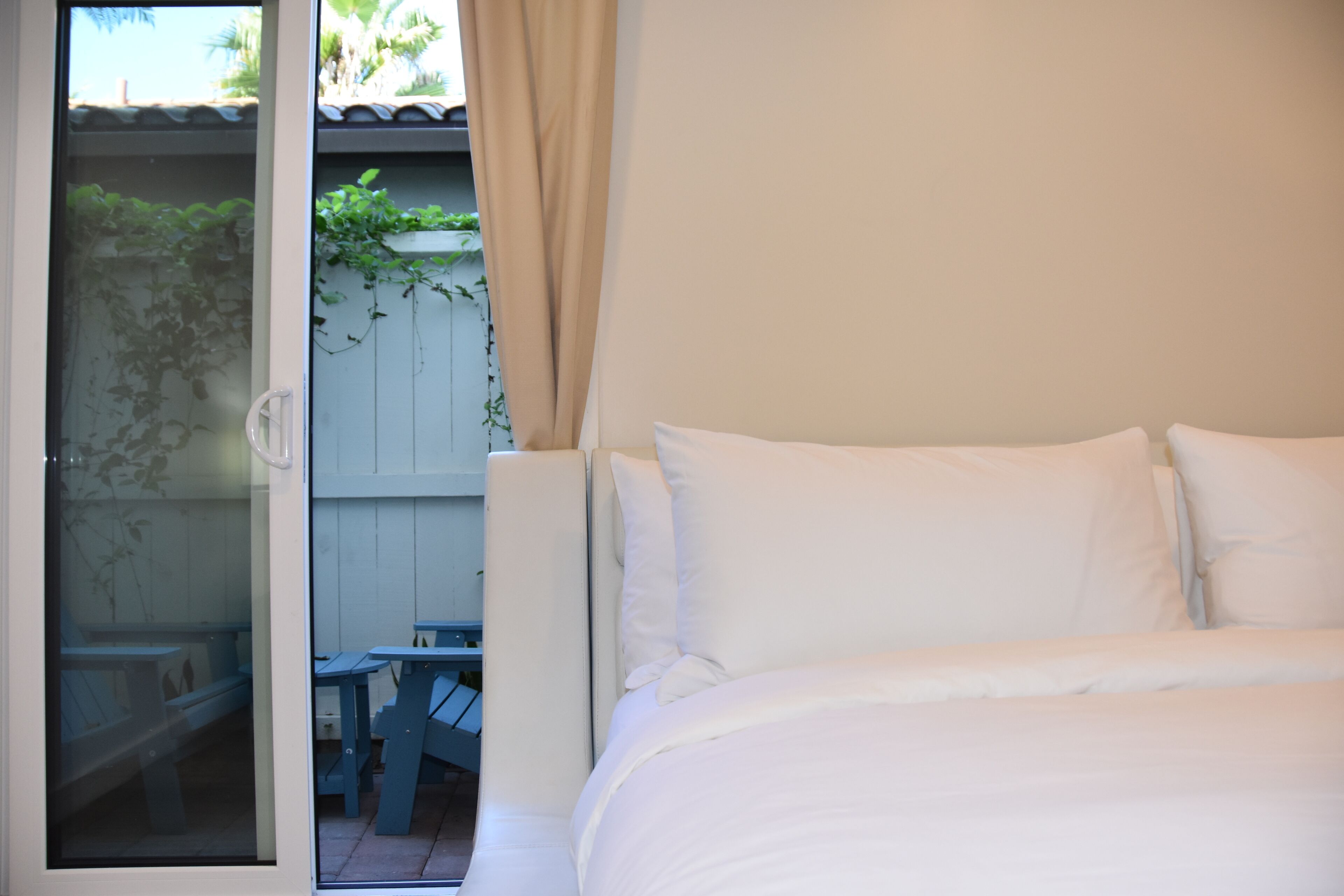 Ein Schlafzimmer mit Bett, einem Fenster mit Vorhängen und Blick auf einen Außenbereich mit Tisch und Stühlen.