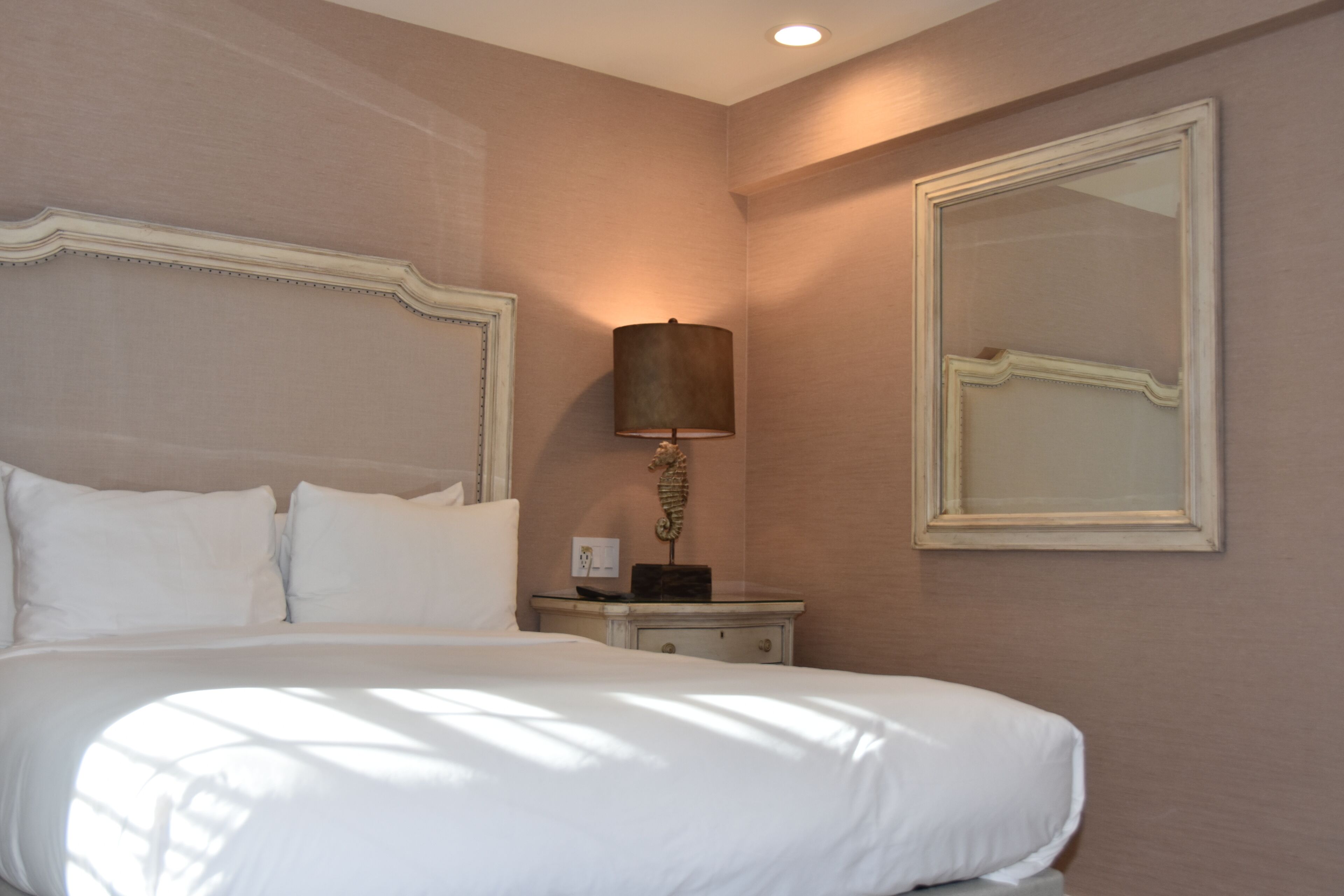 A hotel room with a large bed, a bedside lamp, a mirror, and a nightstand.
