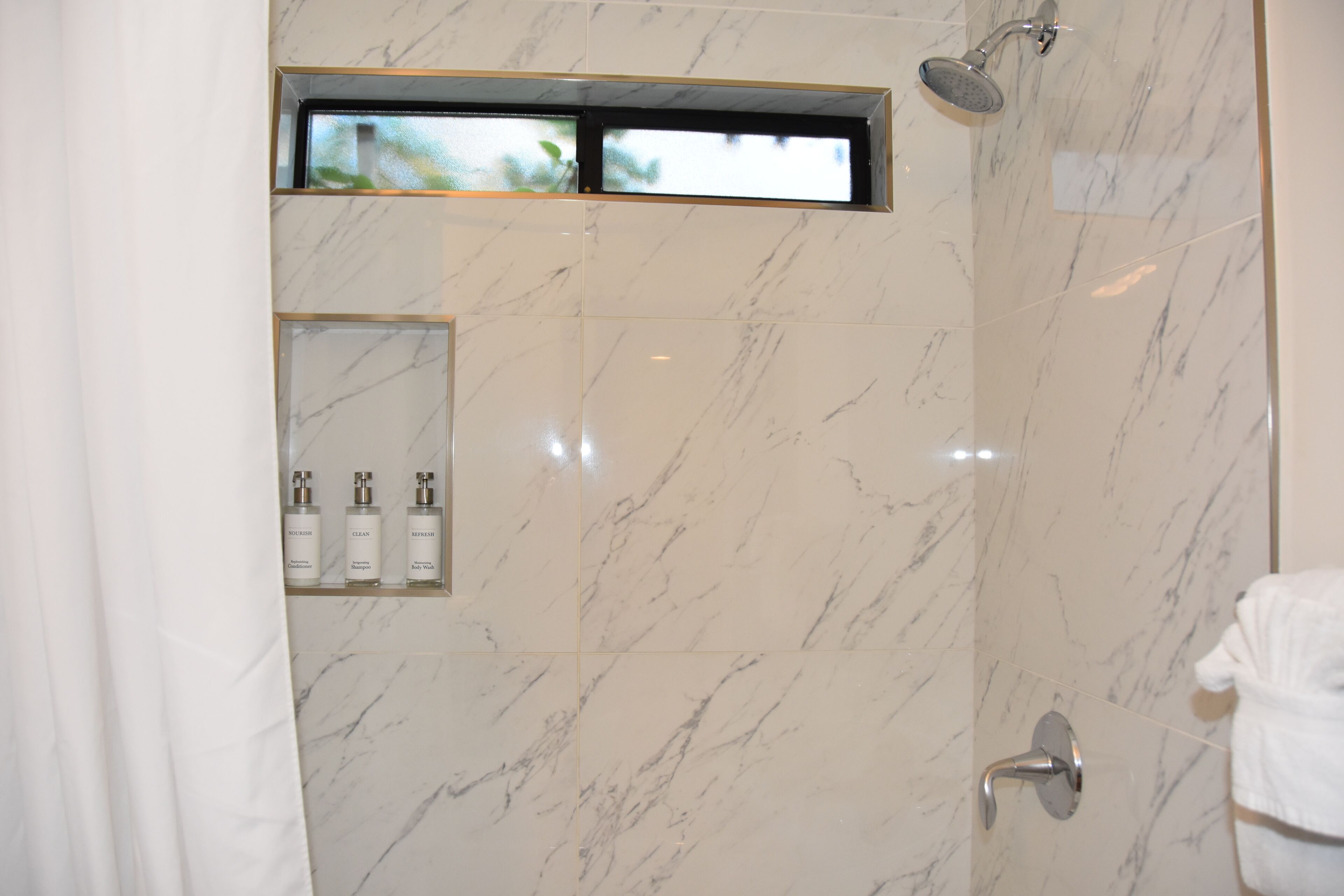 A modern bathroom with a shower, a small window, and a shelf with toiletries.