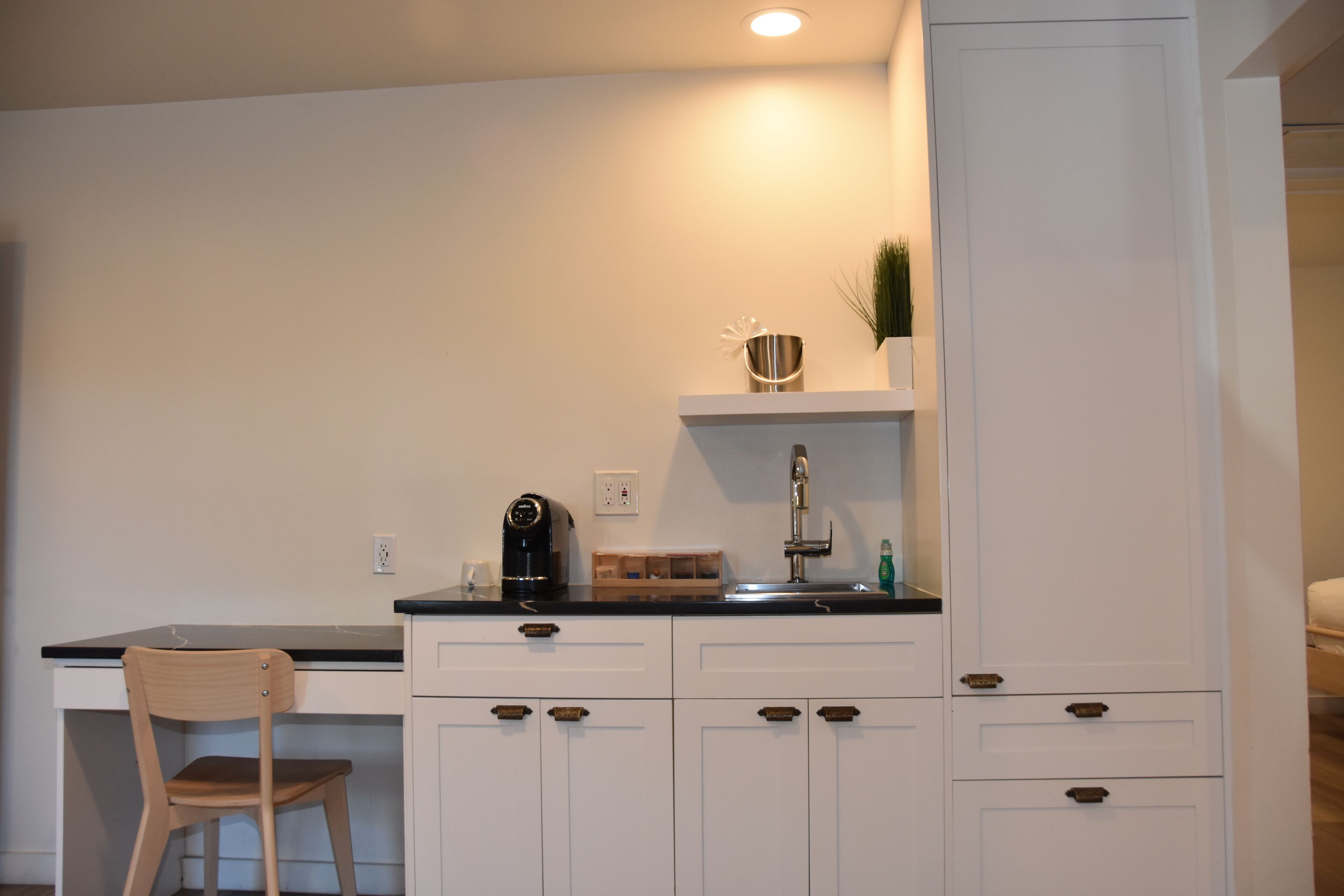 A kitchen with white cabinets, a black countertop, a wooden chair, and a coffee maker.