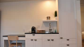 A kitchen with white cabinets, a black countertop, a wooden chair, and a coffee maker.